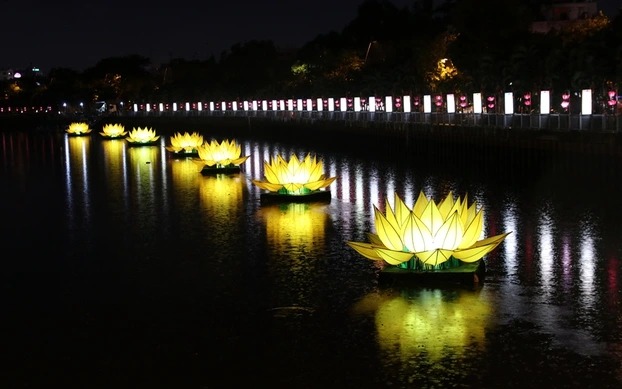 Illuminated lotus lanterns floating on a lake during a Buddhist festival